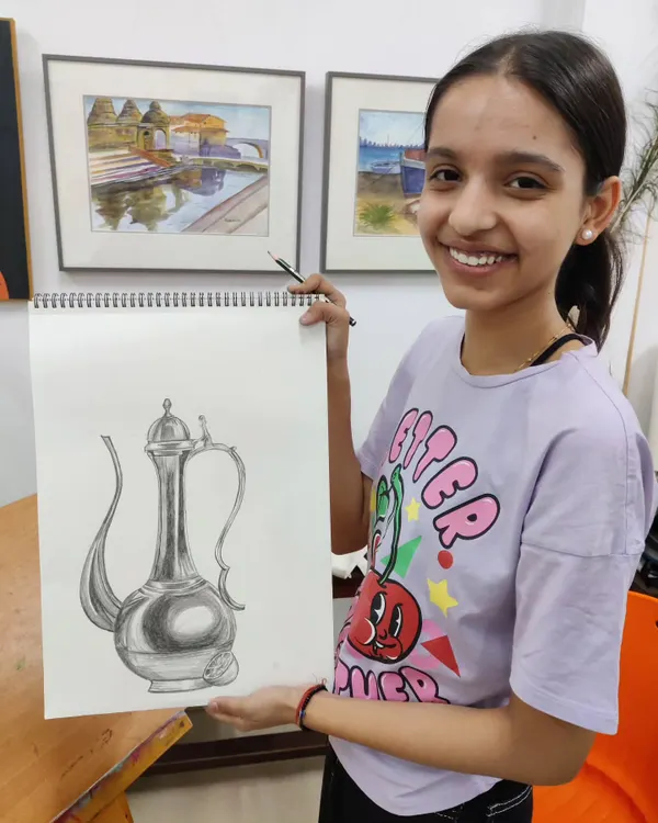 A student proudly shows her completed still life drawing of a metallic jug, demonstrating excellent skill in pencil shading to create realistic textures and reflections.