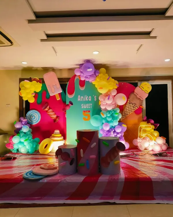 A super sweet ice cream and candy theme for a 5th birthday. The colorful setup includes cutouts of ice cream cones and popsicles, themed plinths, and a light-up number '5', creating a fun Candyland atmosphere.