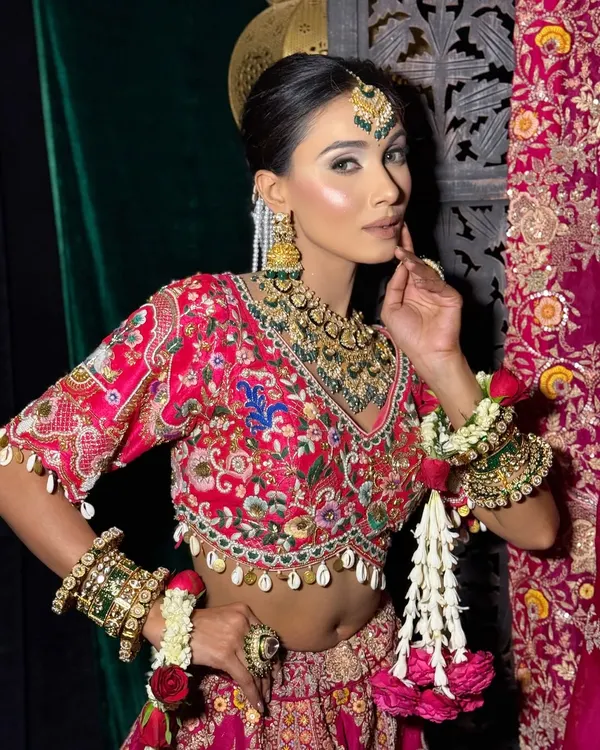 This is a classic Indian bridal look, featuring a sharp, winged eyeliner and a glowing, sculpted base. The makeup is designed to complement the heavy embroidery of the lehenga and the traditional polki jewellery.