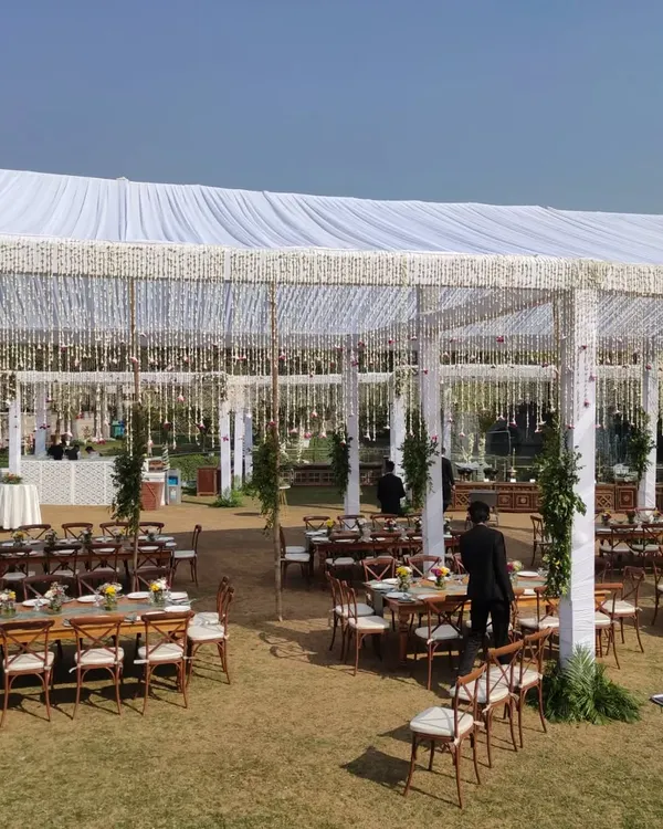 This is a beautiful daytime setup under a large white canopy in a farmhouse. I used hanging floral chandeliers and rustic cross back chairs to create an elegant, alfresco dining experience for the wedding guests.