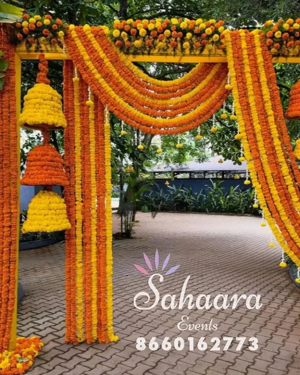A stunning entrance for a Haldi ceremony. This arch is decorated with bright orange and yellow marigold garlands and hanging floral bells, creating a festive and traditional welcome for guests.