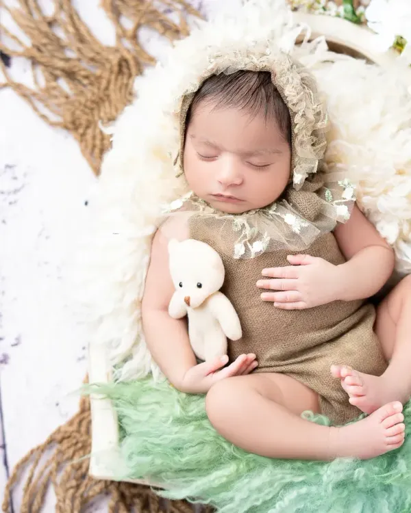 A peaceful newborn rests with a tiny teddy bear, styled with soft, earthy tones and textures. This classic newborn pose highlights the baby's delicate features in a safe and comfortable setting.