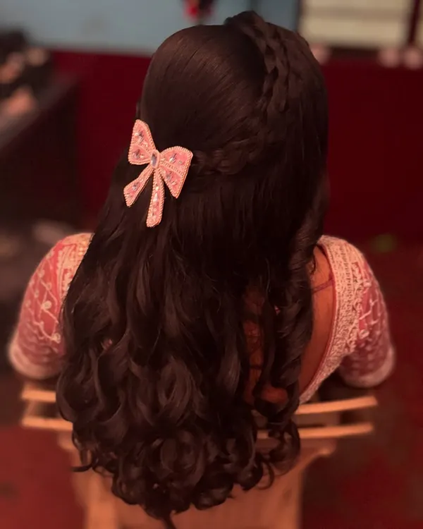 A romantic half-up, half-down hairstyle with soft curls. The look is finished with a delicate, sparkling bow, making it perfect for a reception or engagement party.