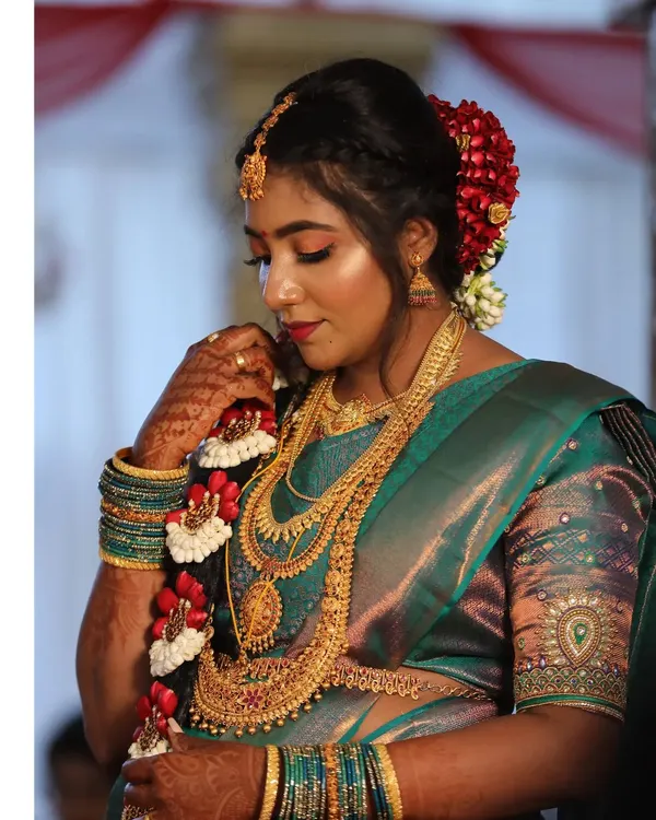 A detailed view of a classic South Indian bridal braid. It is adorned with traditional red and white flowers, creating a beautiful and customary hairstyle that pairs perfectly with a silk saree.