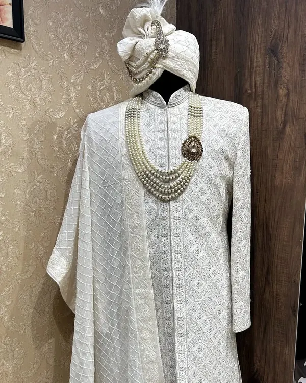A complete royal ensemble. This off-white Chikankari sherwani is paired with a matching safa (turban) and stole, accessorized with a pearl mala and brooch for a classic, coordinated groom's look.