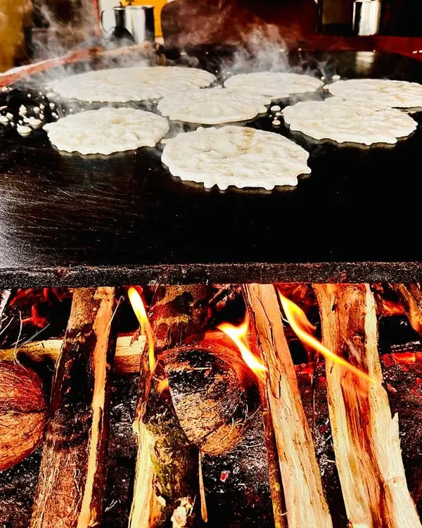 We believe in the power of traditional cooking. Here, akki rotti is being prepared on a large, wood-fired griddle, a method that imparts a unique smoky flavour that cannot be replicated by modern equipment.