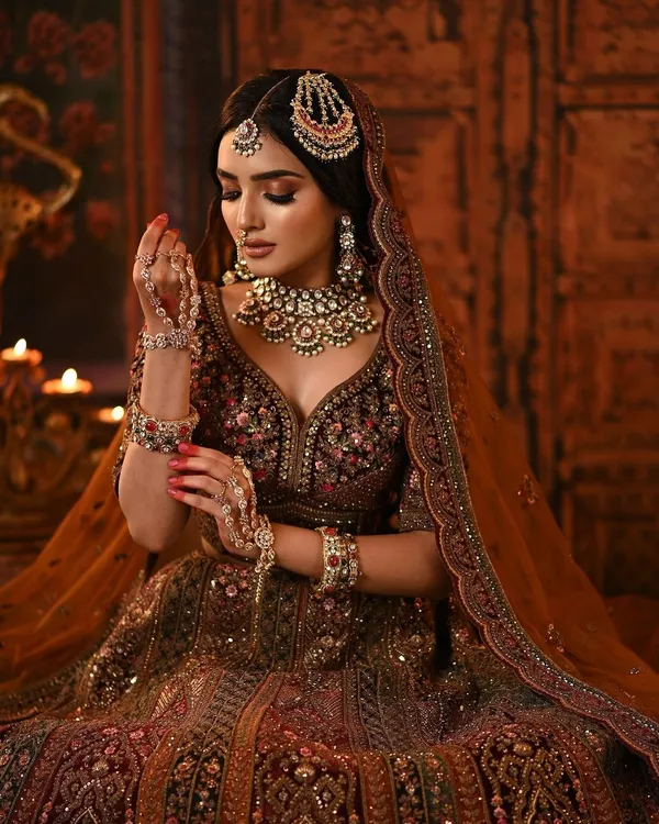 A masterpiece of bridal artistry. This bride's maroon velvet lehenga is paired with dramatic smokey eyes, contoured cheeks, and intricate jewelry for a look that is both royal and captivating.