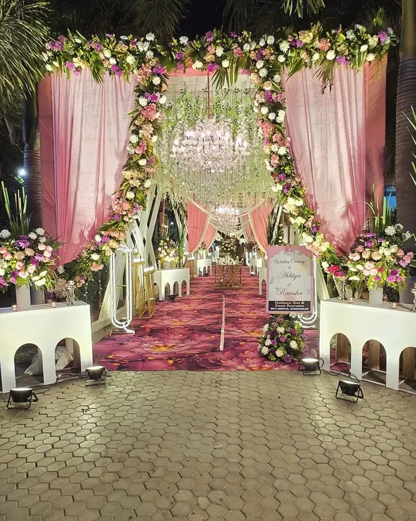 I create grand entrances that set the tone for the entire event. This outdoor wedding walkway features a lush floral arch, elegant pink draping, and a custom printed carpet, all illuminated for a magical evening welcome.
