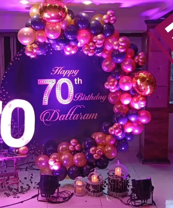 A grand 70th birthday celebration for Dattaram, featuring a deep purple and gold balloon arch, a custom backdrop, and large light-up marquee numbers.