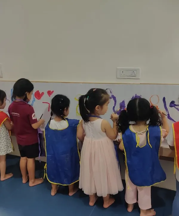 This is what a collaborative art session looks like. A group of children stands side-by-side, each contributing to a large-scale mural, learning to share space and ideas while exploring colors and shapes.
