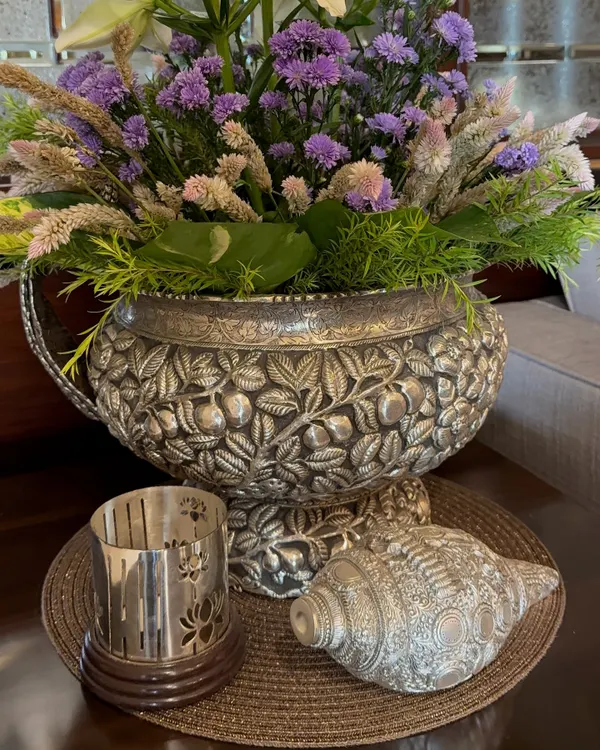 Luxury is in the details. This exquisite silver decorative bowl, intricately carved with floral patterns, is filled with a beautiful arrangement of purple and white flowers, creating a truly opulent centerpiece.