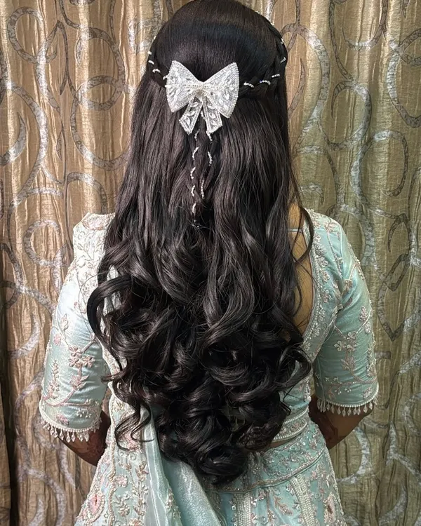 A fairytale hairstyle for a bride. This look features long, flowing curls with a delicate white bow accessory, perfect for a reception or engagement.