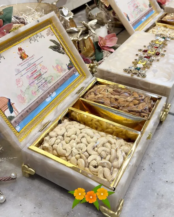 Wedding favors that make a statement. This is a luxury invitation box made of resin, featuring a custom-designed card and compartments for premium cashews and almonds. The top is adorned with intricate jeweled work.