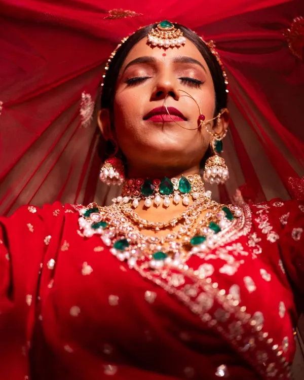 A stunning bridal portrait where the bride is enveloped in her red veil. This shot is all about capturing a moment of serene beauty and the richness of the bridal attire.