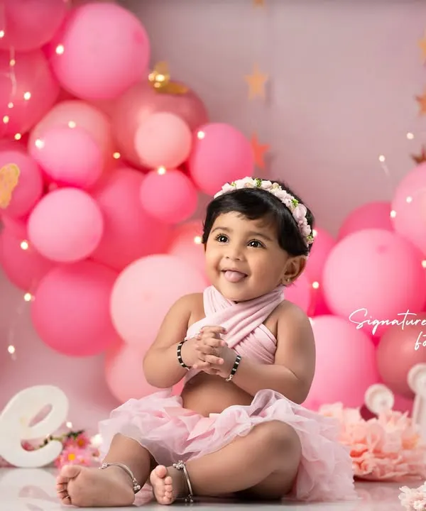 A perfect smile for a first birthday! This little girl is surrounded by a sea of pink balloons and fairy lights in our popular pink-themed cake smash setup. The "One" sign and crown prop add the perfect celebratory touch.