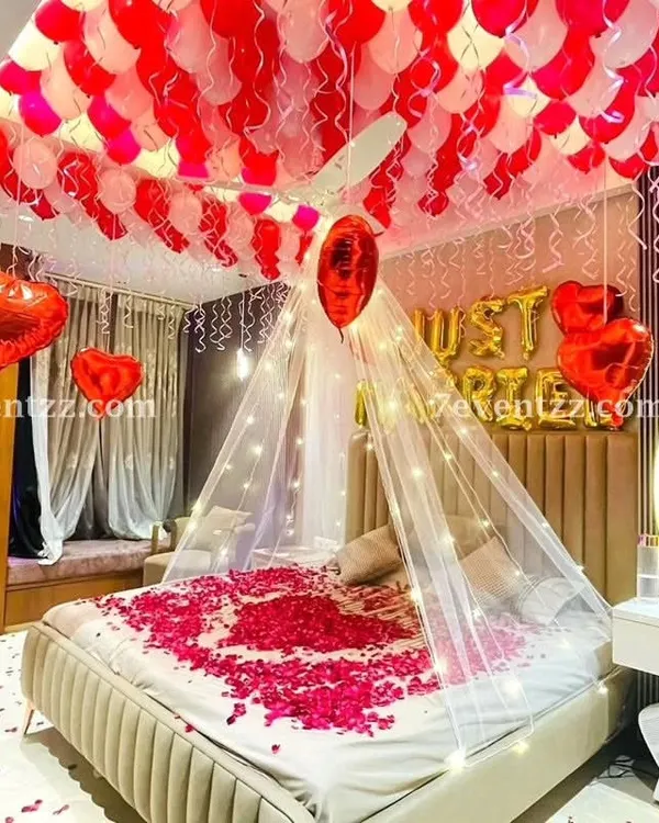 For a truly romantic first night or wedding surprise, I create setups like this one. It features a beautiful canopy over the bed with fairy lights, 'Just Married' foil balloons, and a ceiling full of red and white balloons.