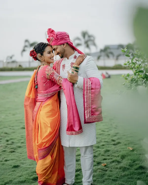 A quiet moment of connection amidst the wedding day buzz. This portrait of a Maharashtrian couple shows the bride in her stunning orange and pink Nauvari saree and the groom in his traditional white sherwani and pink pheta.