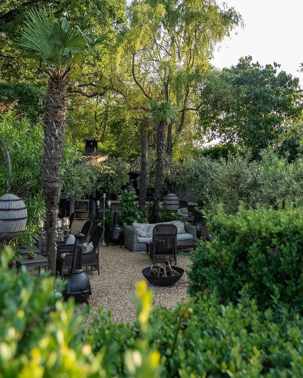 A rustic yet sophisticated outdoor lounge area nestled within a lush garden. We used gravel flooring, comfortable wicker furniture, and a central fire bowl to create an inviting space for gathering with friends and family.