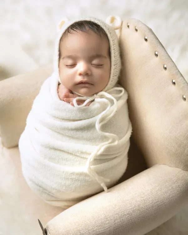A perfectly swaddled newborn sleeping peacefully in a tiny armchair. I love using simple props like this to show just how small and precious they are. The bear-ear bonnet adds a touch of cuteness.