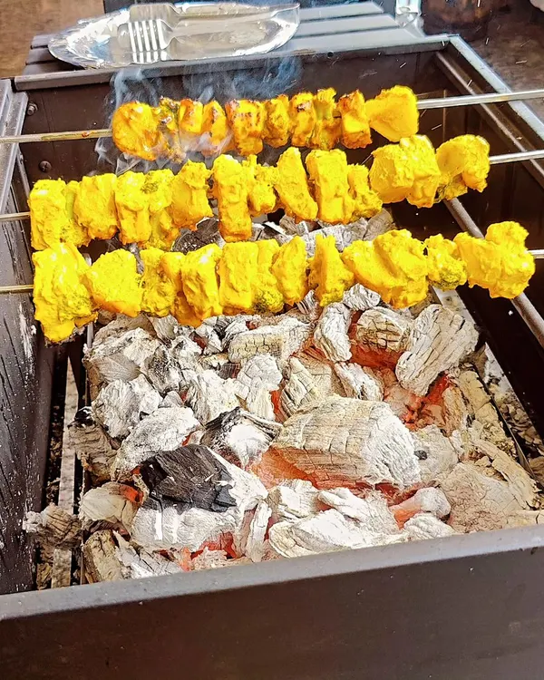 Skewers of marinated paneer and pineapple tikka sizzling over glowing charcoal embers. This close-up shows the delicious char and color we achieve at our live tandoor and barbecue station, a highlight for any event.