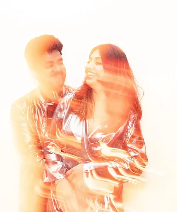 An abstract portrait created with motion blur and warm, orange light flares. The couple is captured in an embrace, their forms blending together in a swirl of color and energy, giving a dreamy, artistic feel.