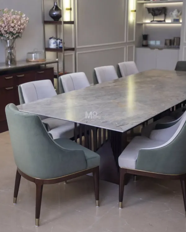 The Aurum Dining Set, featured in a Delhi NCR residence. This table boasts a solid wood top with softly rounded edges, complemented by ergonomically designed chairs in a luxurious two-tone fabric of sage green and neutral grey.
