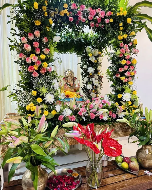 A beautiful and dense floral frame for a home Ganpati celebration. This arrangement is rich with pink and yellow roses, lilies, and anthuriums, creating a full and festive look that surrounds the idol in natural beauty.
