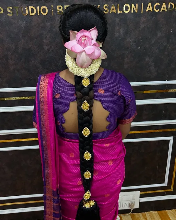 This is my specialty, a traditional South Indian bridal braid. I focus on creating a thick, neat plait, meticulously decorated with classic gold Jadai Billai and topped with a fresh lotus and jasmine flowers, all stitched securely to last through the entire wedding day.