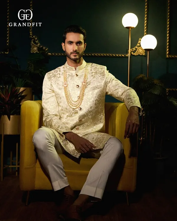 An embodiment of regal sophistication. This bespoke ivory sherwani features intricate hand embroidery and is styled with a traditional pearl necklace, crafted for a groom's most significant moments.