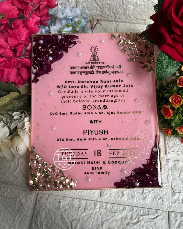 An 8x10 inch resin wedding invitation with a glittery baby pink base. The design features preserved rose petals and stones on diagonal corners, with pearls for an elegant touch.