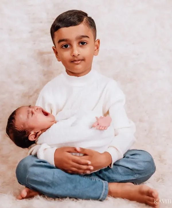 A heartwarming portrait of a big brother proudly holding his newborn sibling. The genuine smile on his face shows the love and excitement of his new role.