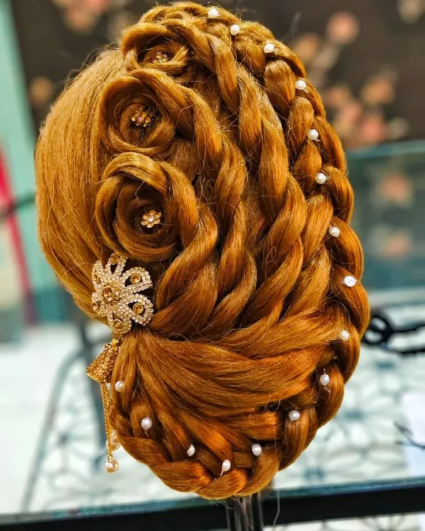 An intricate braided updo with rose details and pearl accents, created by a student on a mannequin head.
