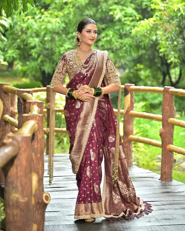 A regal Maharashtrian bride in a deep magenta Nauvari saree, featuring a classic bun, gold jewellery, and green bangles.