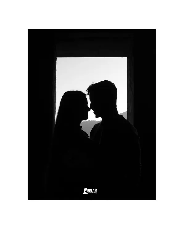 A silhouette of the couple against a window, framed by darkness. This minimalist and artistic shot focuses purely on their connection and the outline of their love.