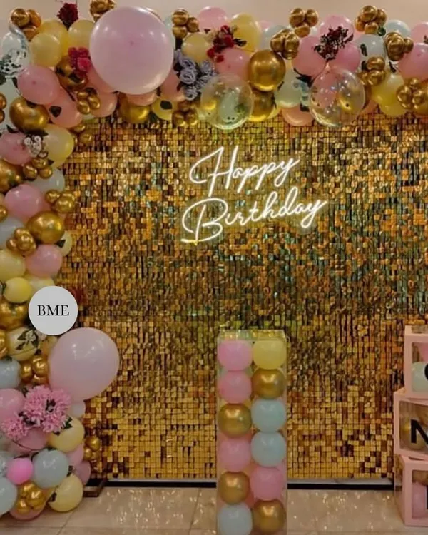 A glamorous birthday decoration with a golden sequin wall. The setup is framed by a pastel balloon arch and includes 'ONE' display boxes, perfect for a stylish first birthday party.