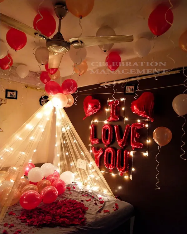 A perfect blend of cozy and romantic, this bed canopy is created with sheer fabric and fairy lights. The setup is completed with "I LOVE YOU" foil balloons and a mix of red and white balloons for a classic expression of love.