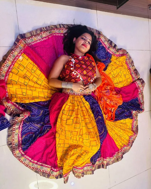 An artistic top-down shot of a model lying down, with her colorful Garba lehenga spread out in a perfect circle. This showcases the vibrant colors and wide flare of my chaniya choli collection.
