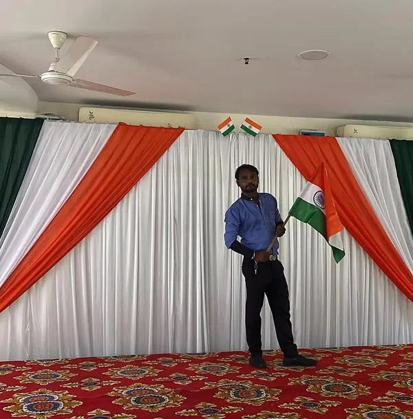 A stage setup for an Independence Day celebration, featuring a backdrop with the tricolor drapes and Indian flags.