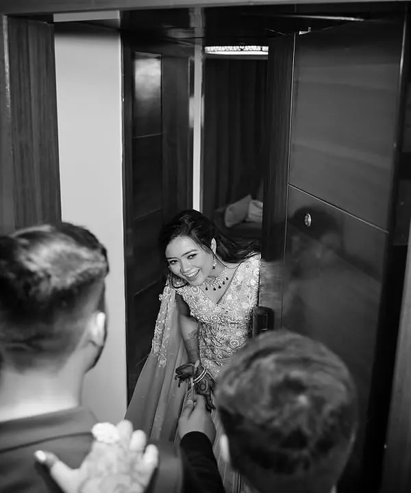 A candid moment captured in monochrome. The bride peeks out from a doorway with a joyful laugh, and the black and white treatment emphasizes the raw emotion and happiness of the moment.