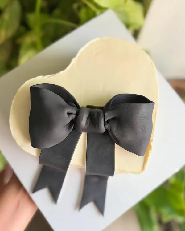Minimal, chic, and timeless. This heart-shaped buttercream cake is topped with a single, perfectly sculpted black fondant bow for a modern and sophisticated romantic statement.