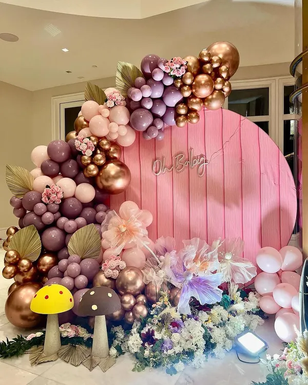 A wide view of the whimsical woodland baby shower setup. The round pink backdrop with the "Oh Baby" sign is framed by a lush balloon garland in shades of mauve and rose gold, with mushroom props adding a touch of fairytale magic.