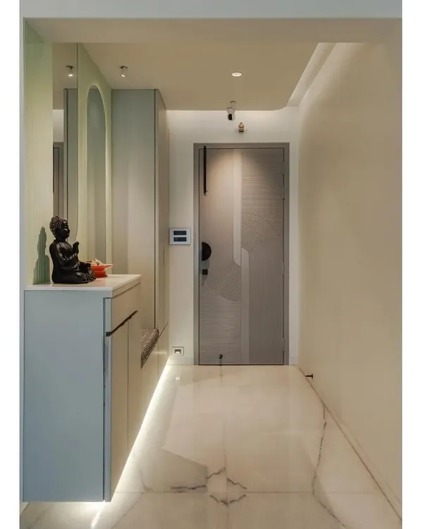 This entryway features a floating console in a sophisticated grey matte laminate, providing storage right by the door. The design is enhanced by a pastel green accent wall, an arched mirror, and cove lighting for a warm and inviting welcome.