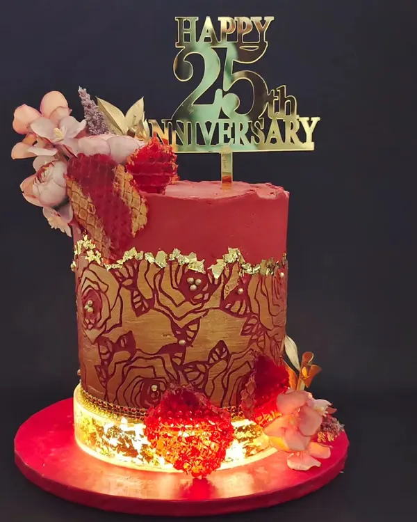A stunning cake for a 25th anniversary, glowing with its own internal light. The design features a rich red and gold color scheme with a rose-stenciled pattern and edible, jewel-like isomalt hearts.