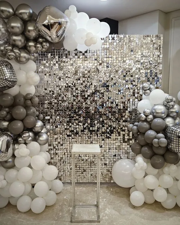 A full view of the silver shimmer wall decoration. Framed by white, grey, and silver balloons with disco ball accents, this backdrop is perfect for a glamorous party.