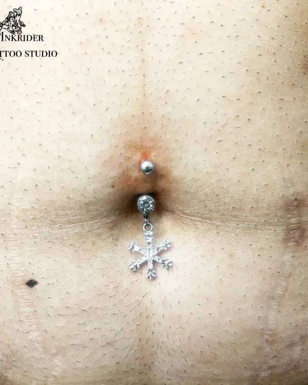 A festive navel piercing with a dangling snowflake charm, perfect for adding a unique touch. I have a wide selection of jewelry, including crystal and charm barbells.