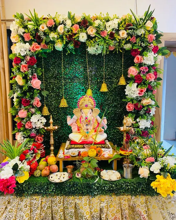 We created this serene Ganpati mandap using a lush green backdrop to make the colorful flowers pop. The arch is decorated with a mix of pink, red, and white roses, with traditional brass bells hanging for a divine touch.