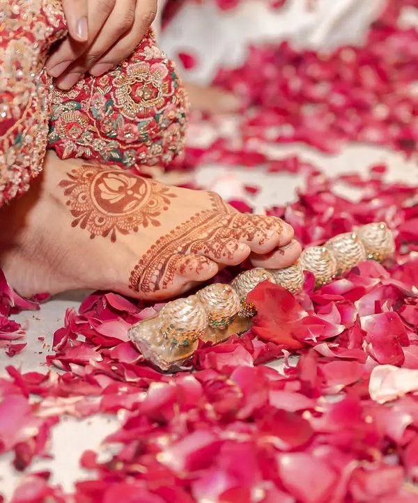 Sometimes the smallest details tell the biggest stories. A bride's feet, adorned with intricate mehendi and toe rings, step onto a bed of soft rose petals. It’s a poetic frame that signifies the beginning of her new journey.
