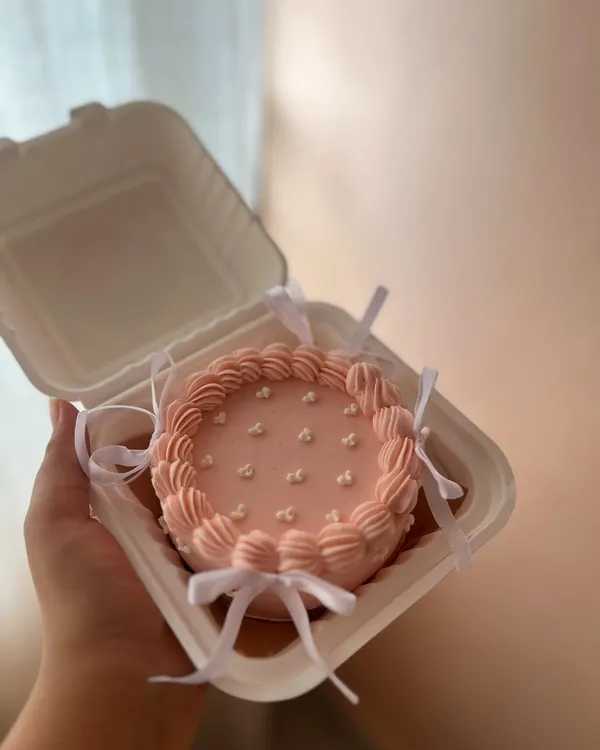 A pretty pink bento cake with delicate piping and tiny white bows. This is a great example of a simple, coquette-style design for a personal treat.