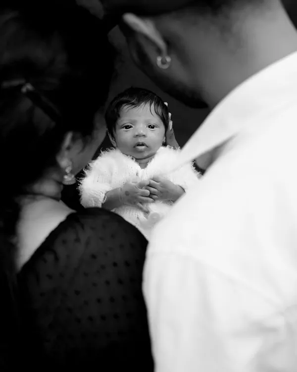 A powerful black and white portrait of a newborn looking right at the camera, held securely in their parents' arms. This image is all about connection and love.
