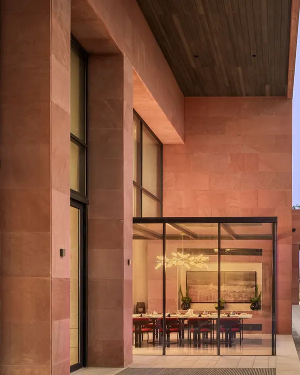 The exterior of the Elevate Clubhouse in Gurugram, where a glass-encased dining room creates a seamless connection between the interior and the landscaped outdoors. The use of red sandstone and large transparent surfaces establishes a modern yet warm architectural presence.